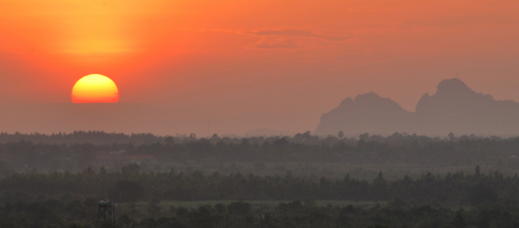 orange sun setting over horizon and mountains.