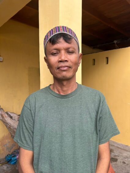 man in green shirt in front of yellow building looking at camera